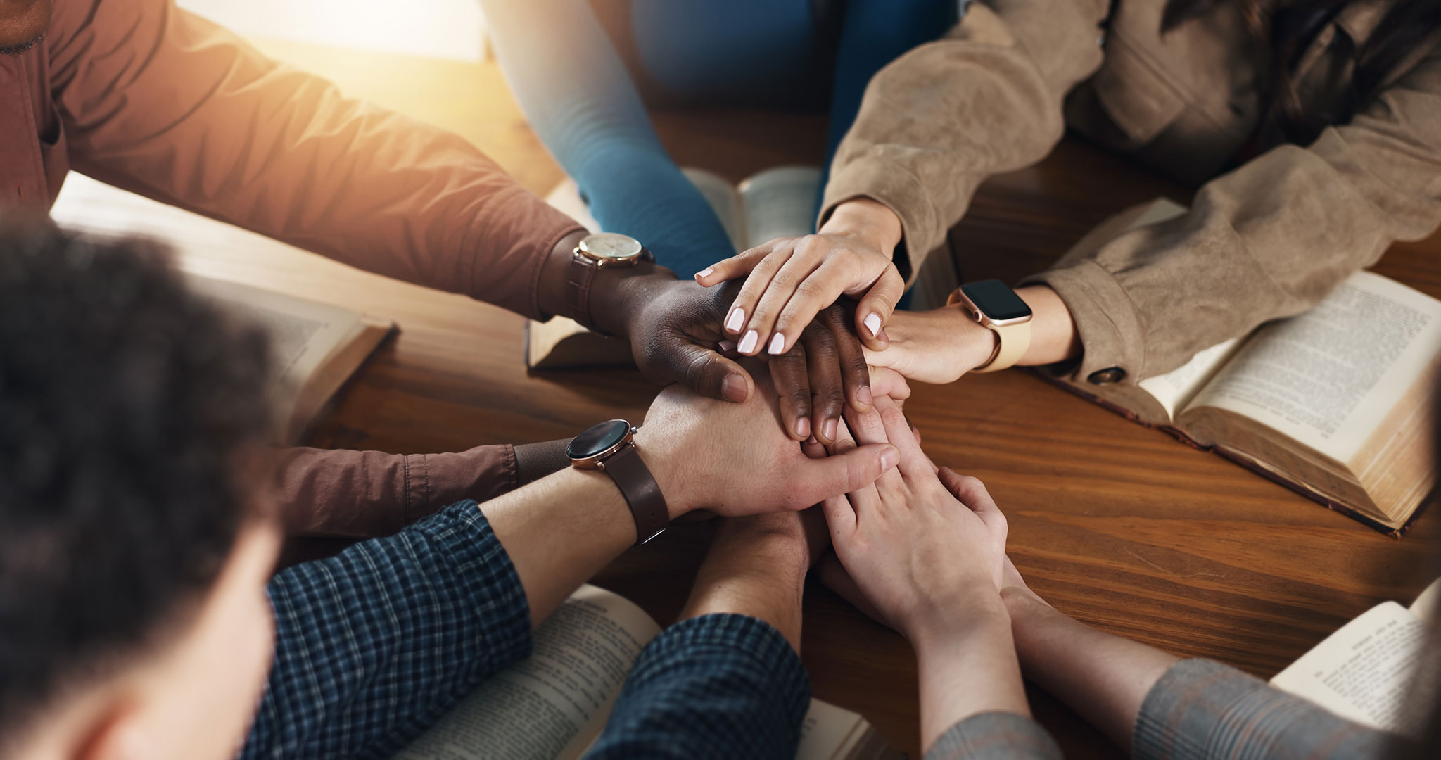 group of people placing hands together on table with Bibles on the table
